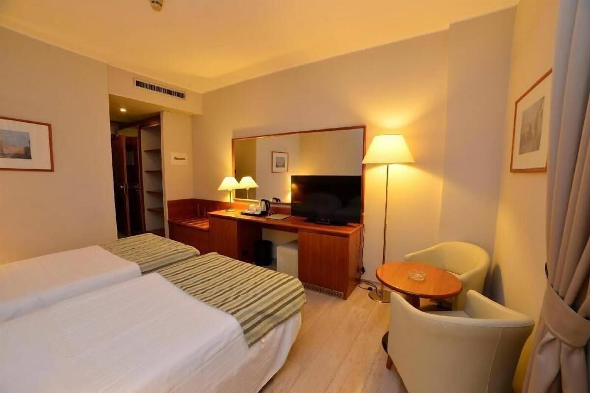A hotel room with two beds, a desk with a television, a chair, and a small table.