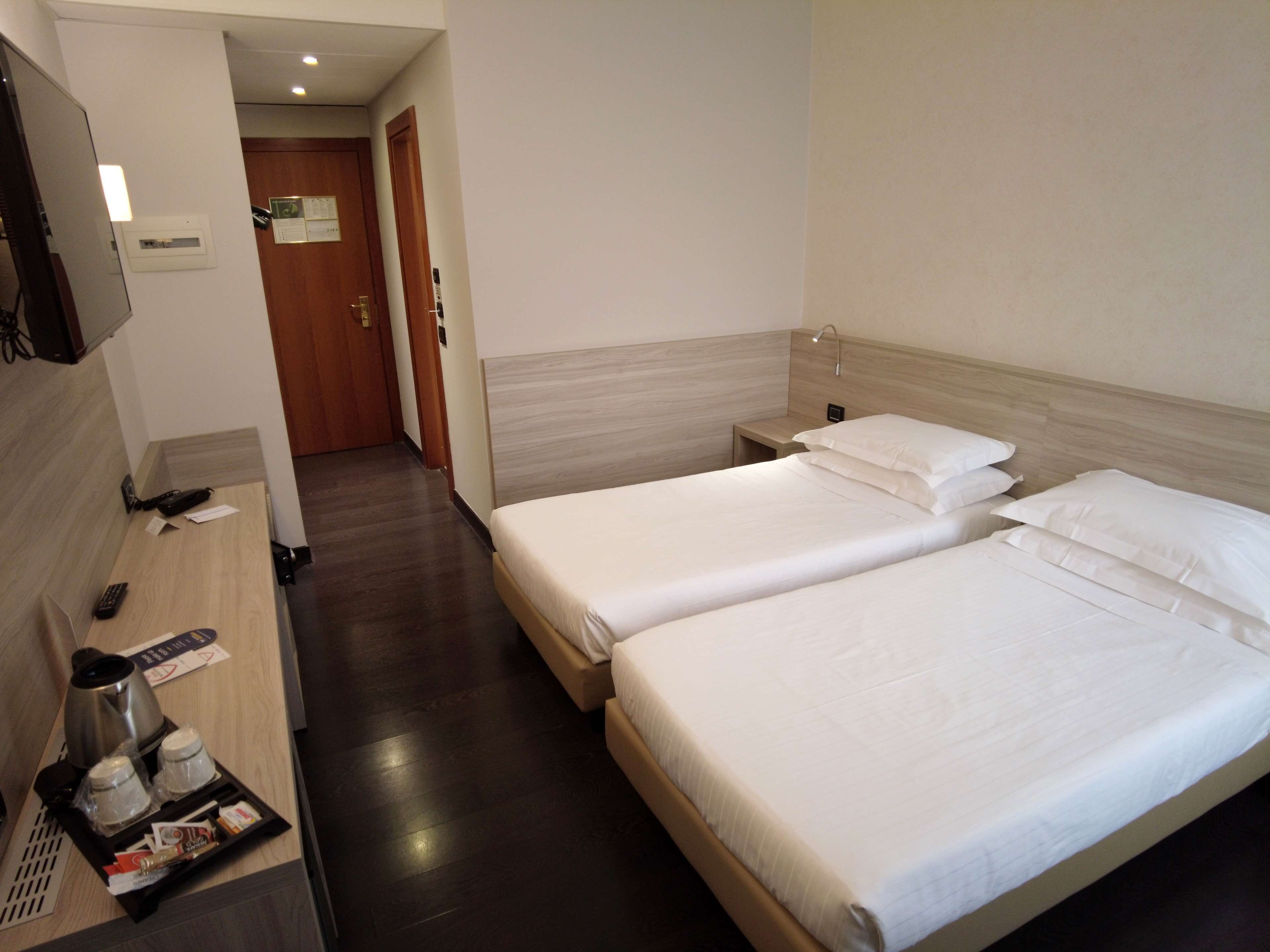 A hotel room with two beds, a desk with a coffee maker, and a TV.