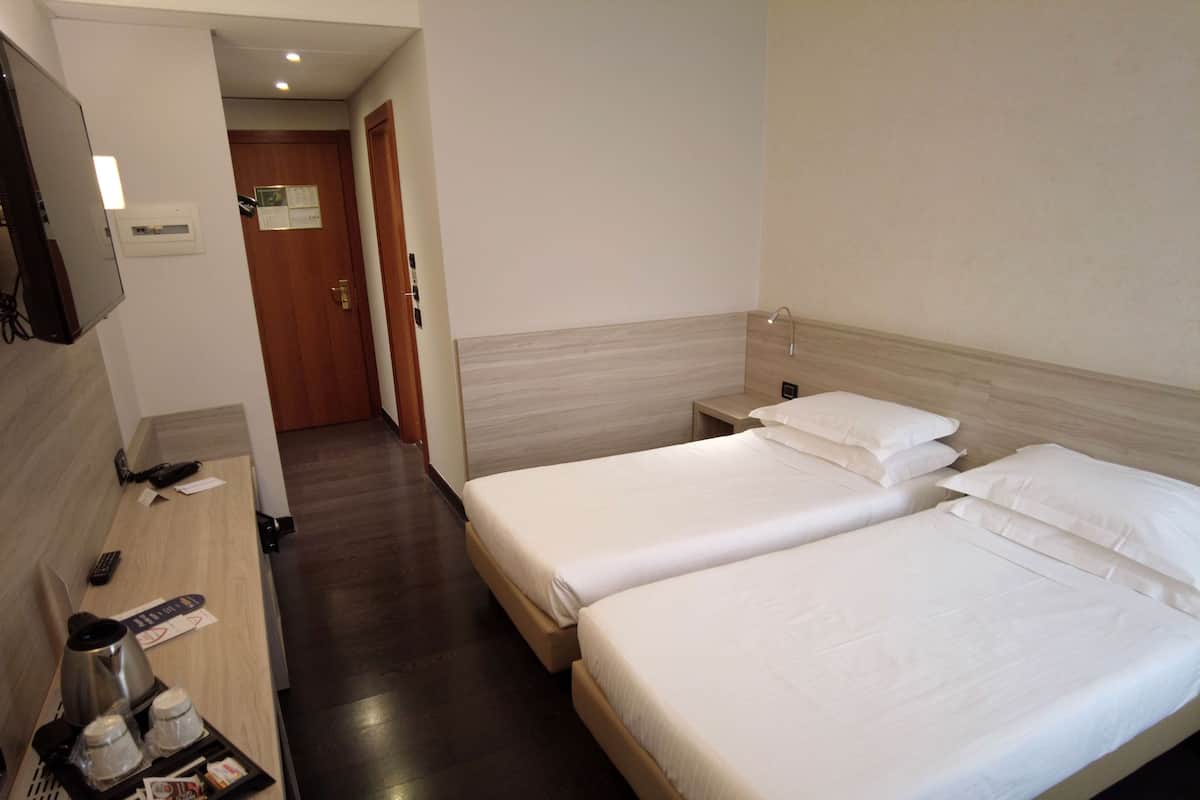 A hotel room with two beds, a desk with a coffee maker, and a TV.