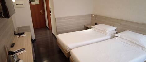A hotel room with two beds, a desk with a coffee maker, and a TV.