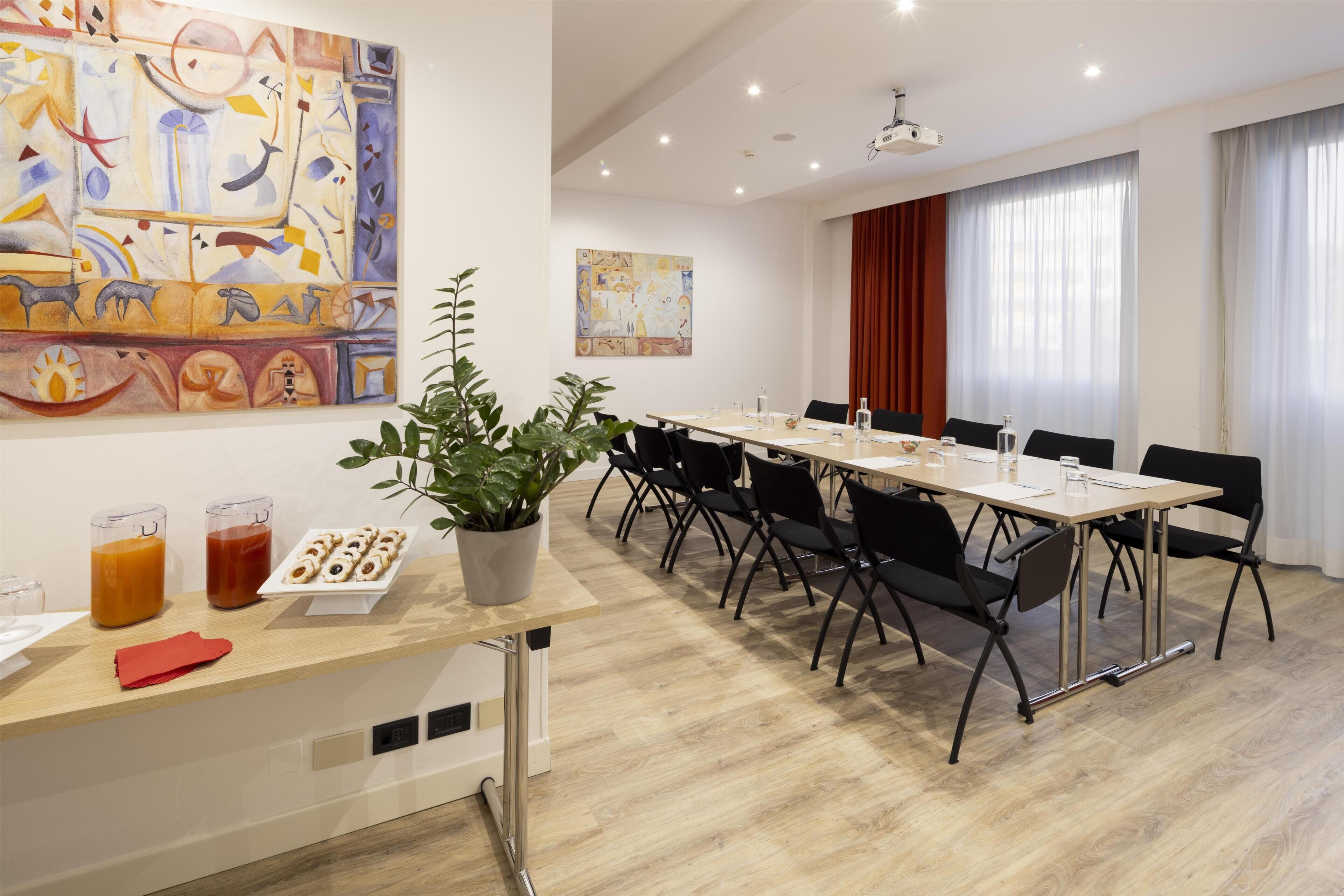 A modern conference room with a long table, black chairs, a potted plant, and abstract art on the walls.
