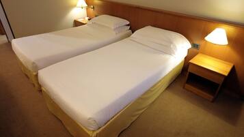 Ein Hotelzimmer mit zwei Einzelbetten, jeweils mit einem hölzernen Kopfteil, einem Nachttisch mit Lampe und einem Teppichboden.