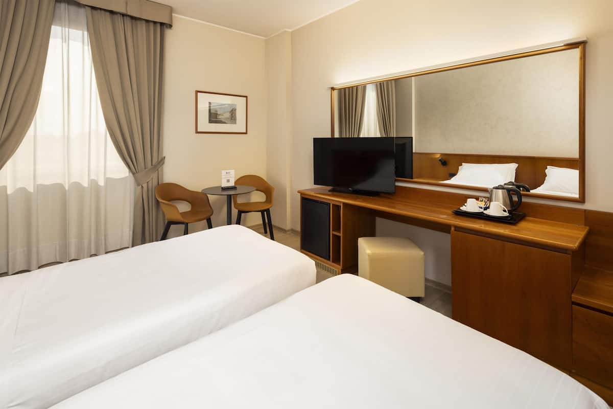 A hotel room with two beds, a desk with a TV, a chair, a small table, and a mirror.