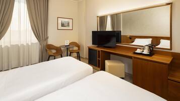 A hotel room with two beds, a desk with a TV, a chair, a small table, and a mirror.