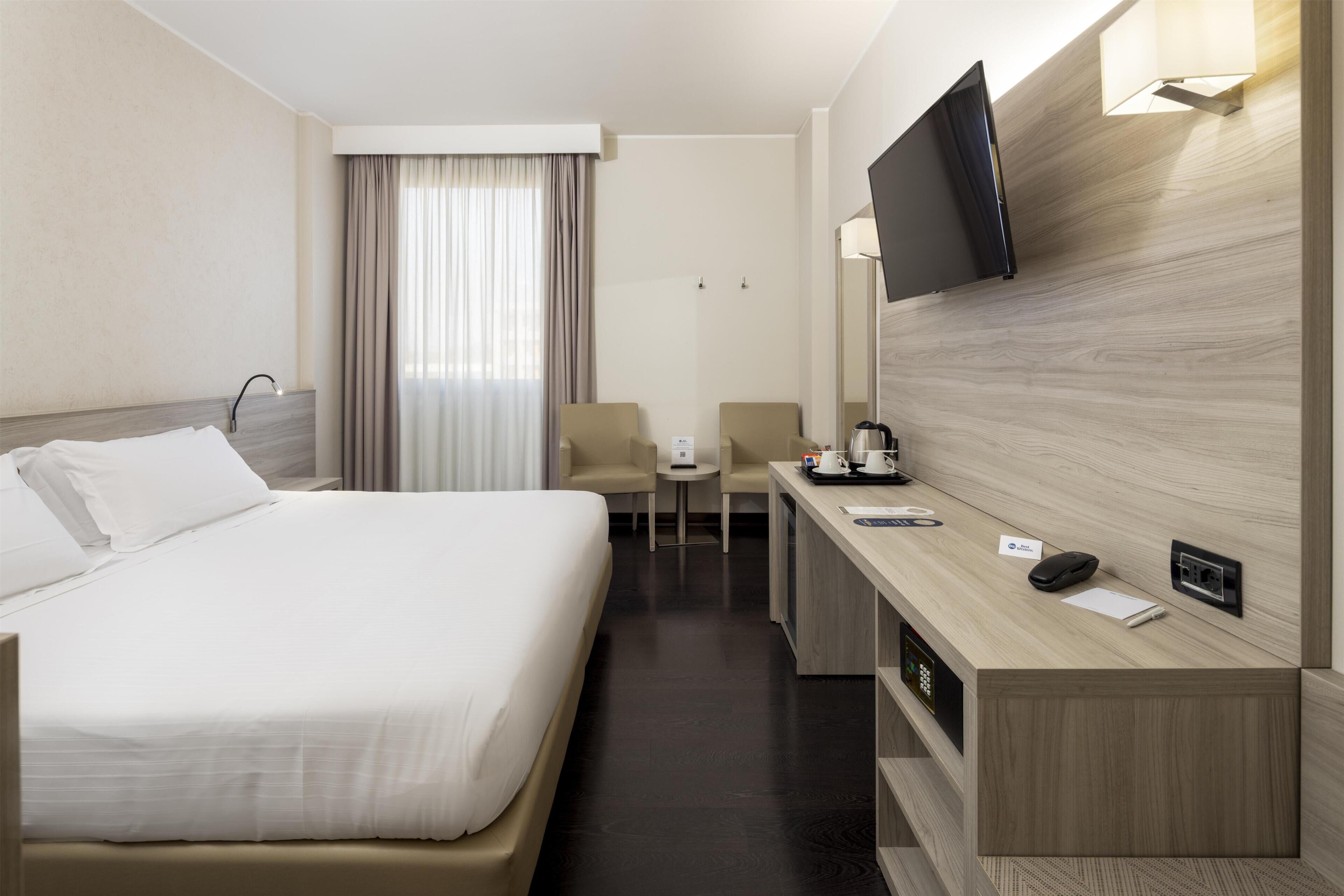 A hotel room with a bed, a desk, a chair, a TV, and a window with curtains.