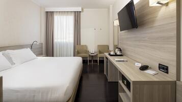 A hotel room with a bed, a desk, a chair, a TV, and a window with curtains.