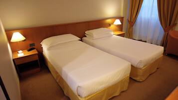 Ein Hotelzimmer mit zwei Einzelbetten, einem Nachttisch mit Lampe und einem kleinen Tisch.