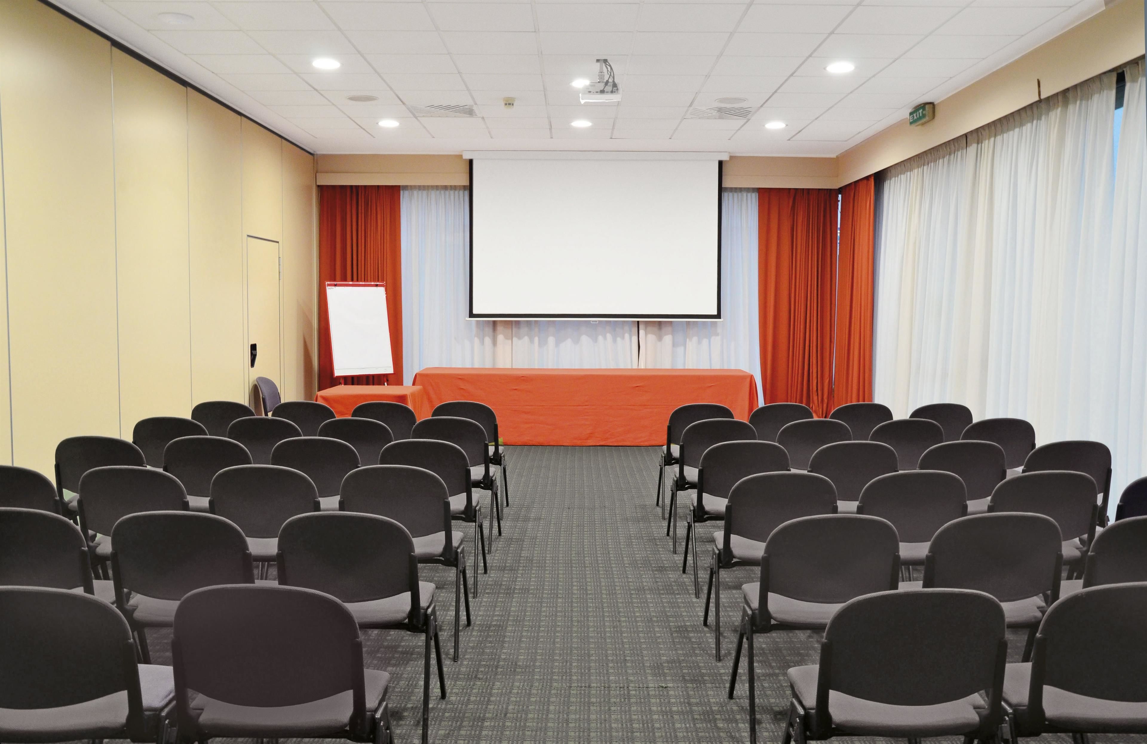 A conference room with rows of chairs, a projector screen, and a presentation screen.