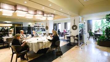 Un comedor amplio con mesas redondas, iluminación en el techo y vistas al exterior.