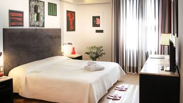 A hotel room with a large bed, a desk with a lamp, a TV, and artwork on the walls.