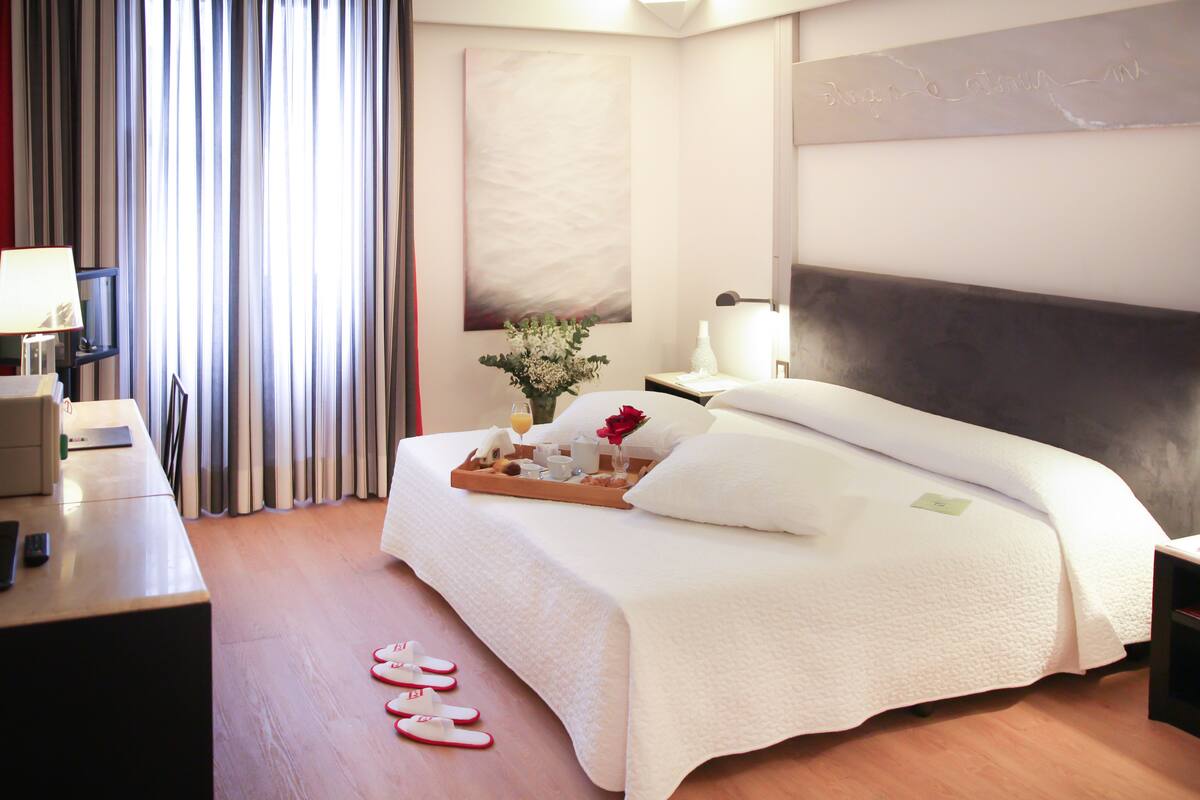 A neatly made bed with a tray of breakfast items, a bedside table with a lamp, and a large abstract painting on the wall.