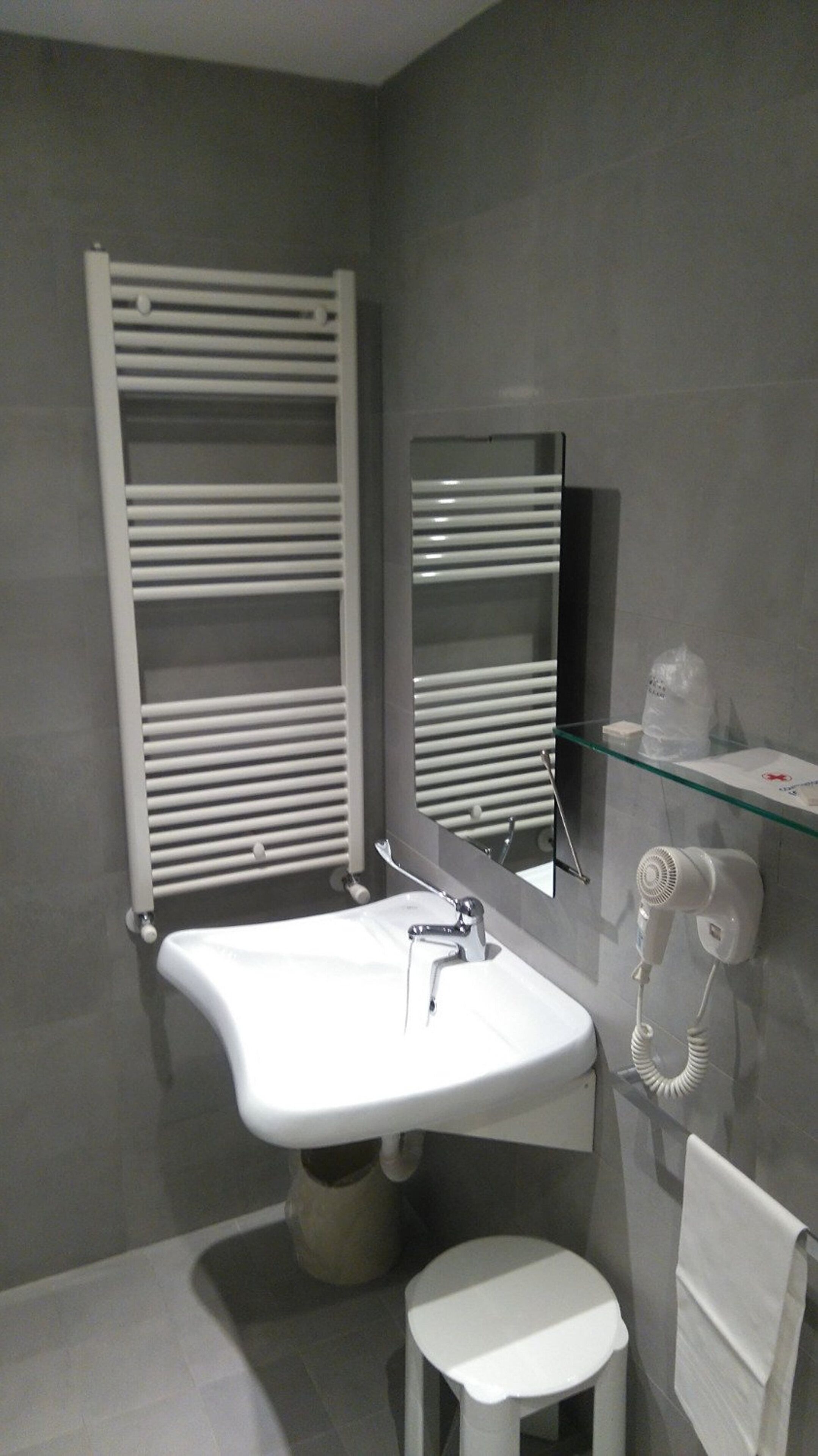 Ein modernes Badezimmer mit Waschbecken, Handtuchhalter, Spiegel und einem Föhn auf einer Glasablage.