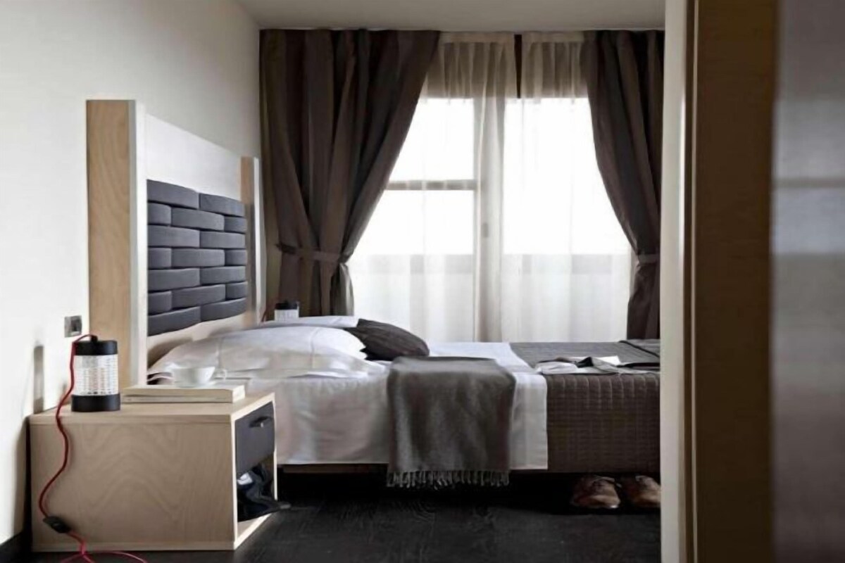 A modern hotel room with a bed, bedside table, and a window with curtains.