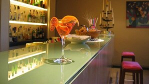 A bar area with a martini glass on the counter, a shelf with bottles, and a painting on the wall. - Art Hotel Museo (Prato)