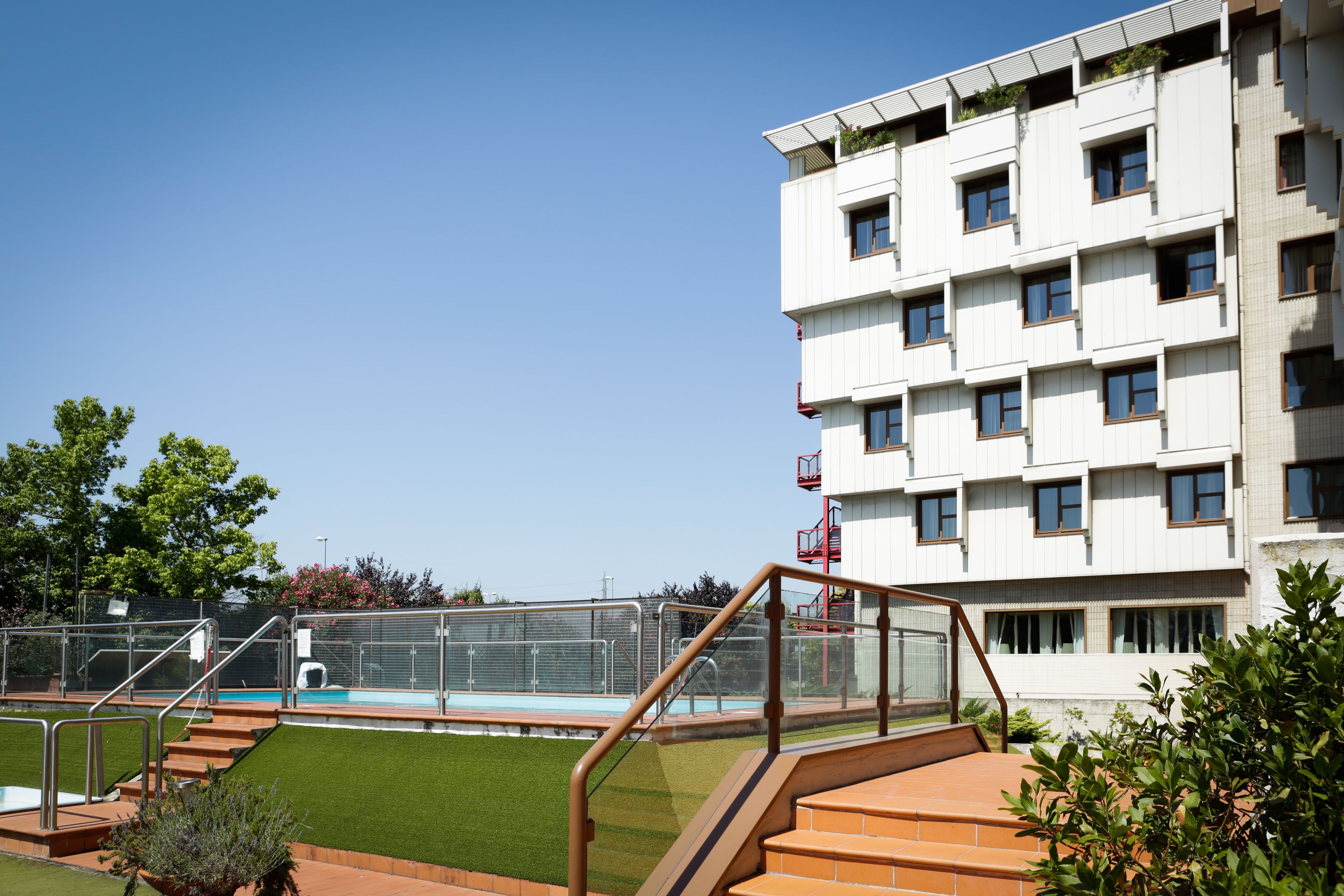 A modern building with a swimming pool, a staircase, and a well-maintained lawn.