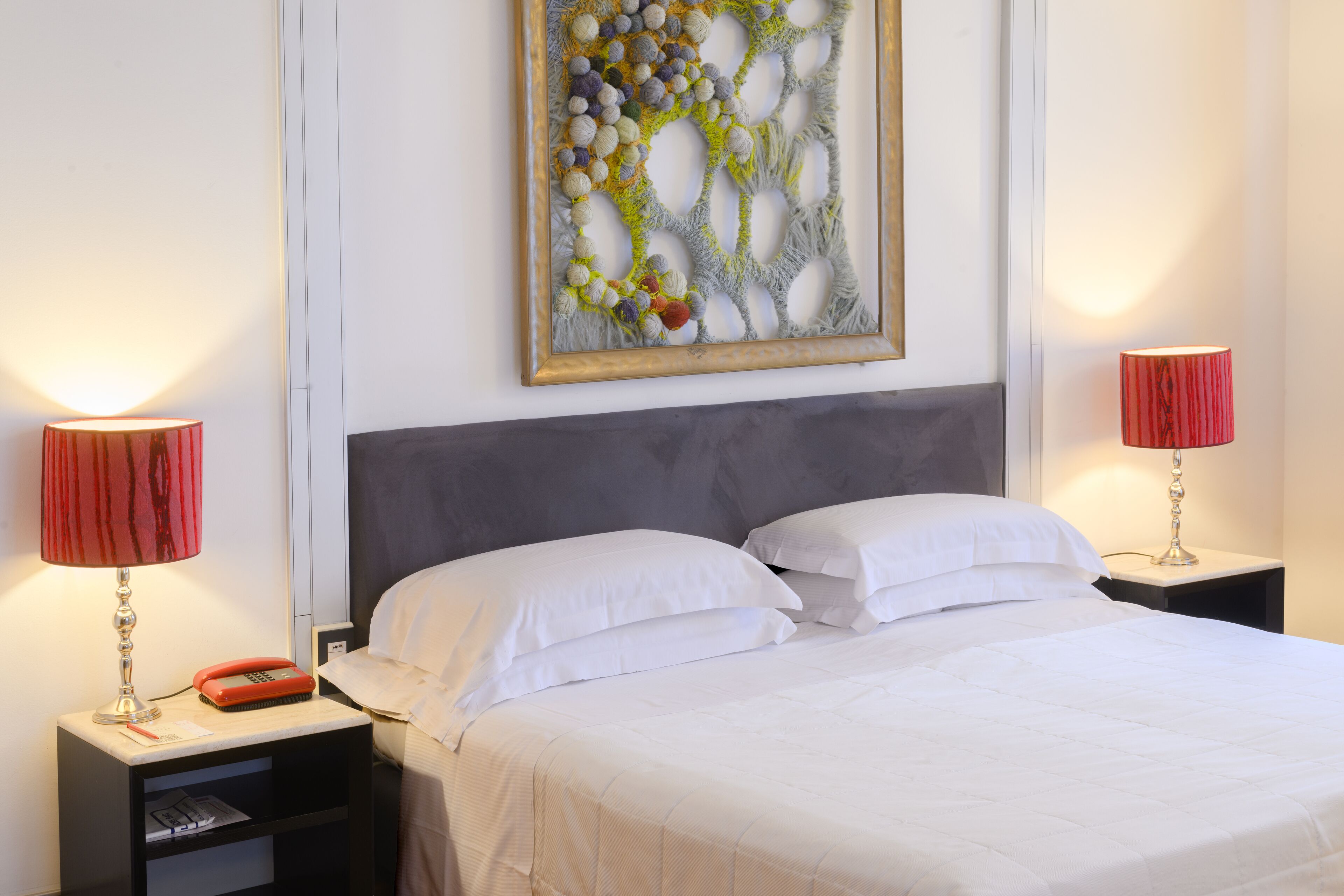 A neatly made bed with white linens, two bedside tables with lamps, and a wall-mounted artwork.