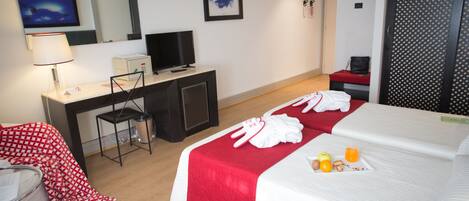A hotel room with a bed, a desk, a chair, a TV, and a red and white checkered blanket.