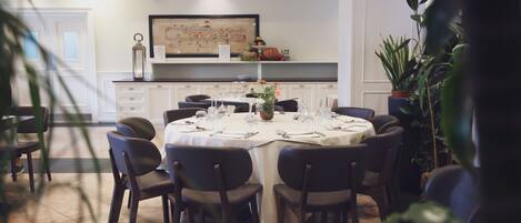 A dining area with a round table set for six, surrounded by chairs, in a room with white walls and a tiled floor.