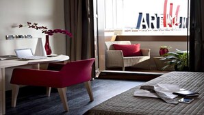 A hotel room with a bed, a desk with a laptop, a chair, a vase with flowers, and a view of the outside. - Art Hotel Museo (Prato)