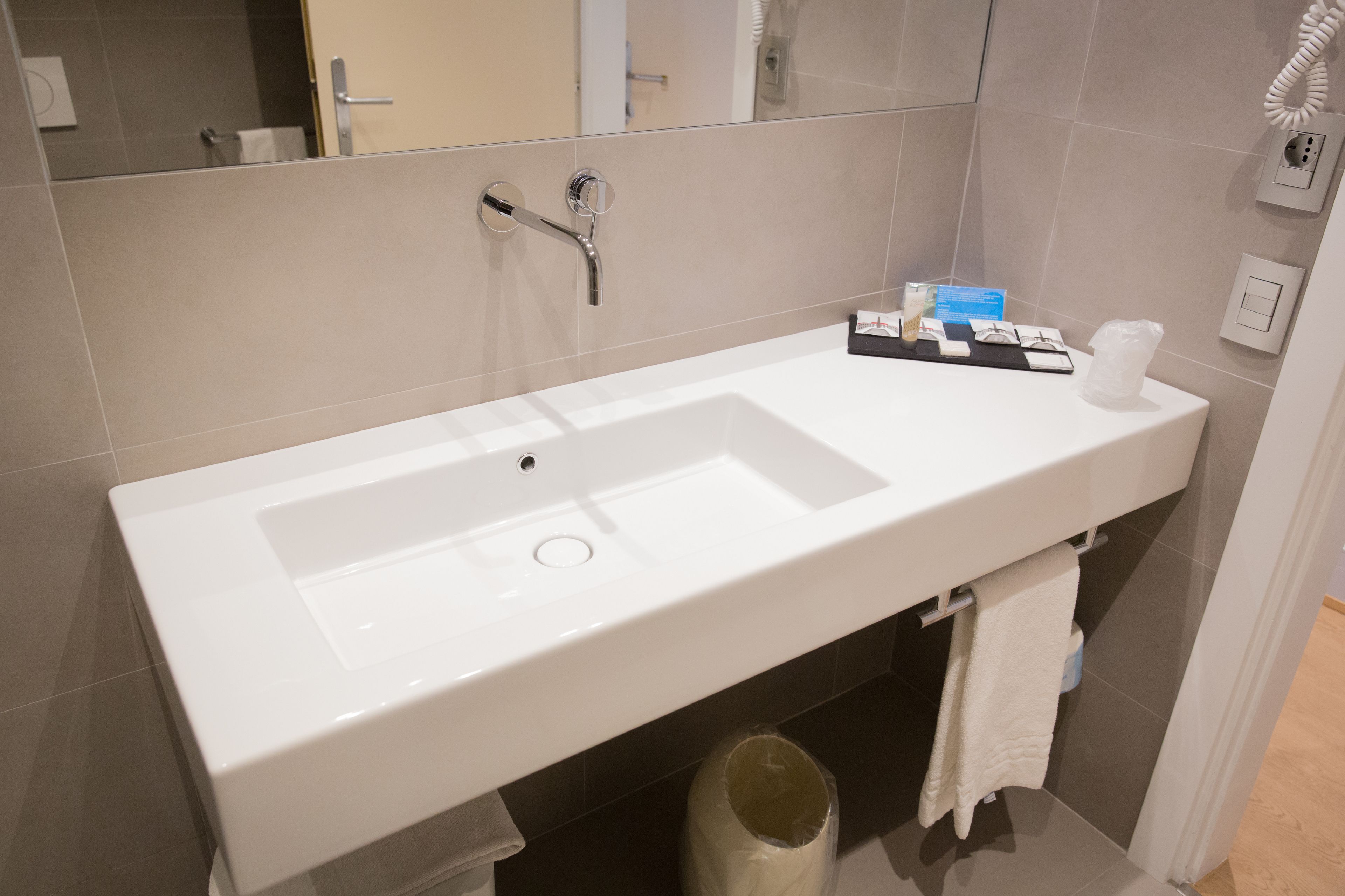 Een moderne badkamer met een witte wastafel, een spiegel en een handdoekrek.