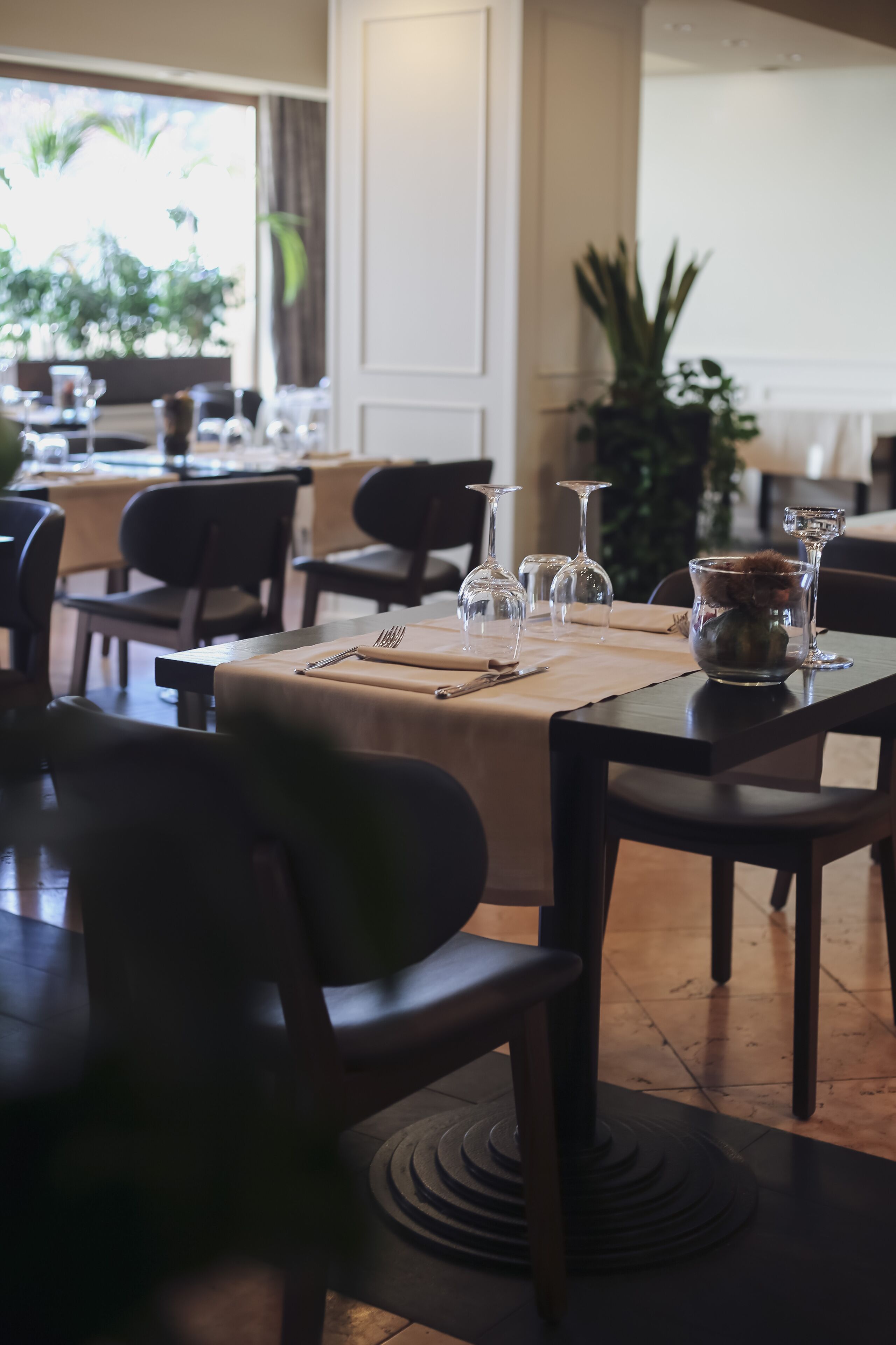 Ein Restaurantinneres mit gedeckten Tischen, Stühlen und einem Blumentopf.