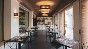 A restaurant with tables set for dining, a kitchen in the background, and large windows allowing natural light. - Art Hotel Museo (Prato)