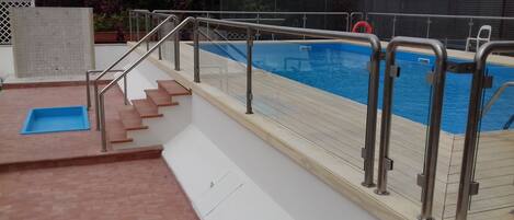 Une piscine dotée d’une terrasse en bois et de rampes en métal.