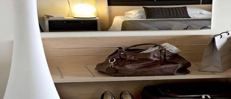 A hotel room with a bed, nightstand, lamp, handbag, shoes, and suitcase.