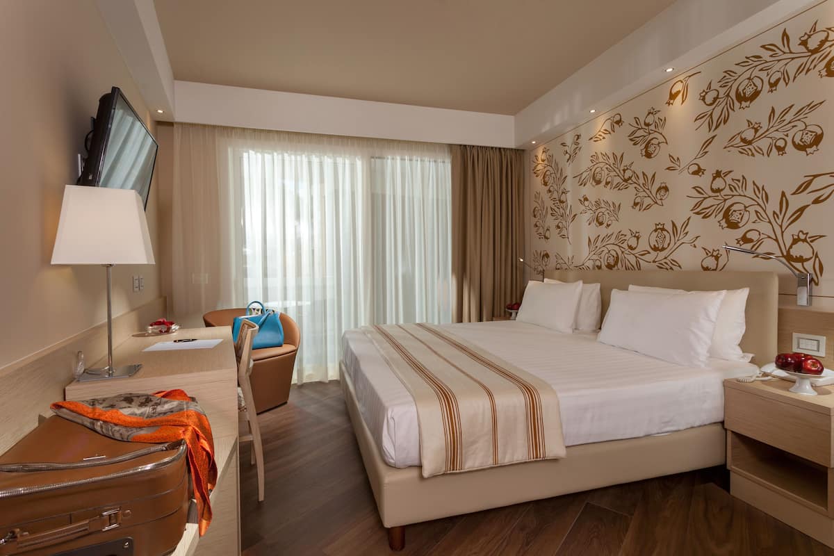 Une chambre d’hôtel avec un grand lit, un bureau, une chaise, une télévision et une fenêtre avec des rideaux.