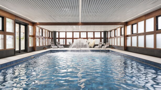 Una piscina interior con una cascada, rodeada de paredes de madera y grandes ventanales.