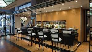 Zona de bar con una barra larga, varios taburetes y una amplia variedad de botellas.