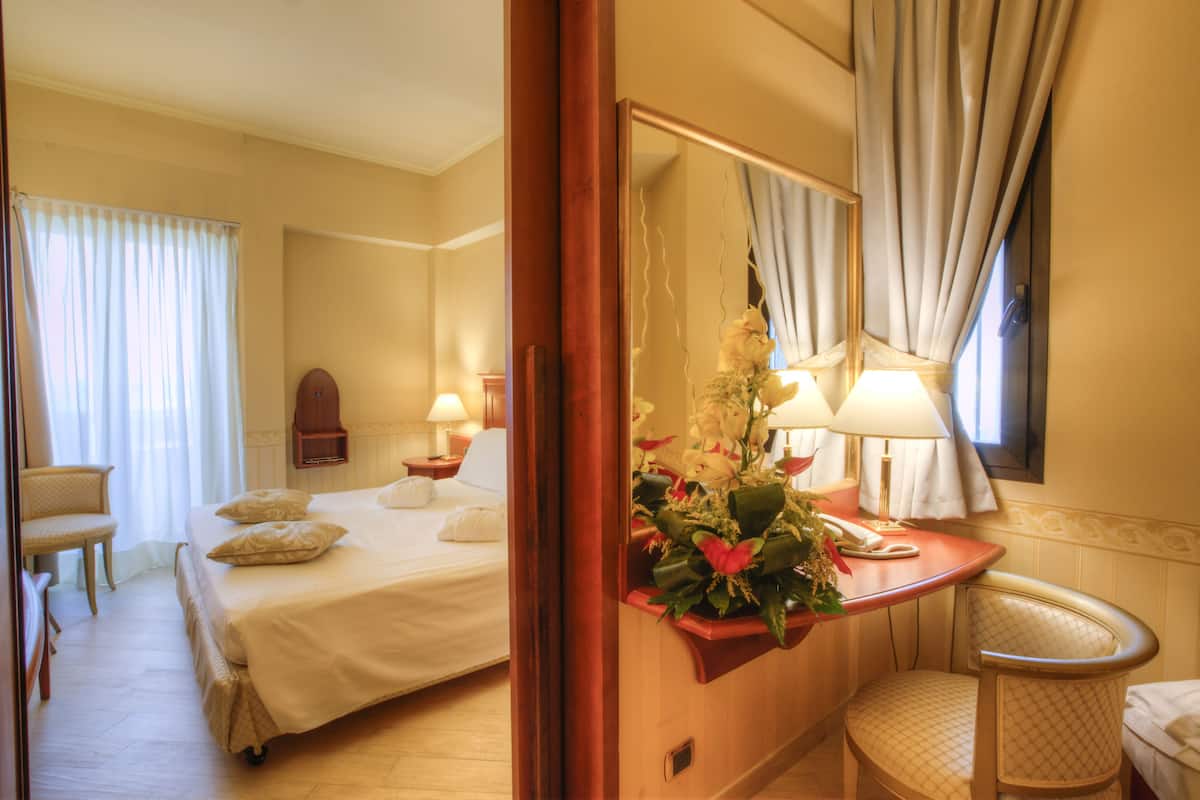 Une chambre d’hôtel avec un lit, un bureau doté d’une lampe, une chaise et un miroir.
