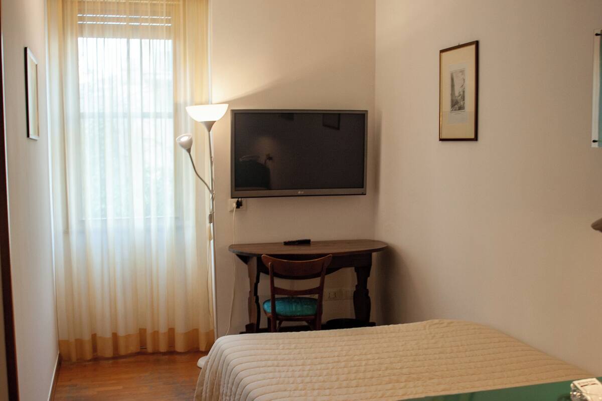 A hotel room with a bed, a desk, a chair, a television, and a window with curtains.