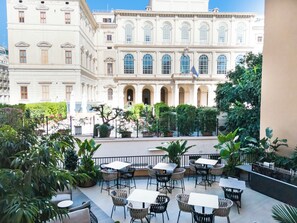 A courtyard with outdoor seating and a large building with arched windows in the background. - Palazzo 4 Fontane 12 (Rome)