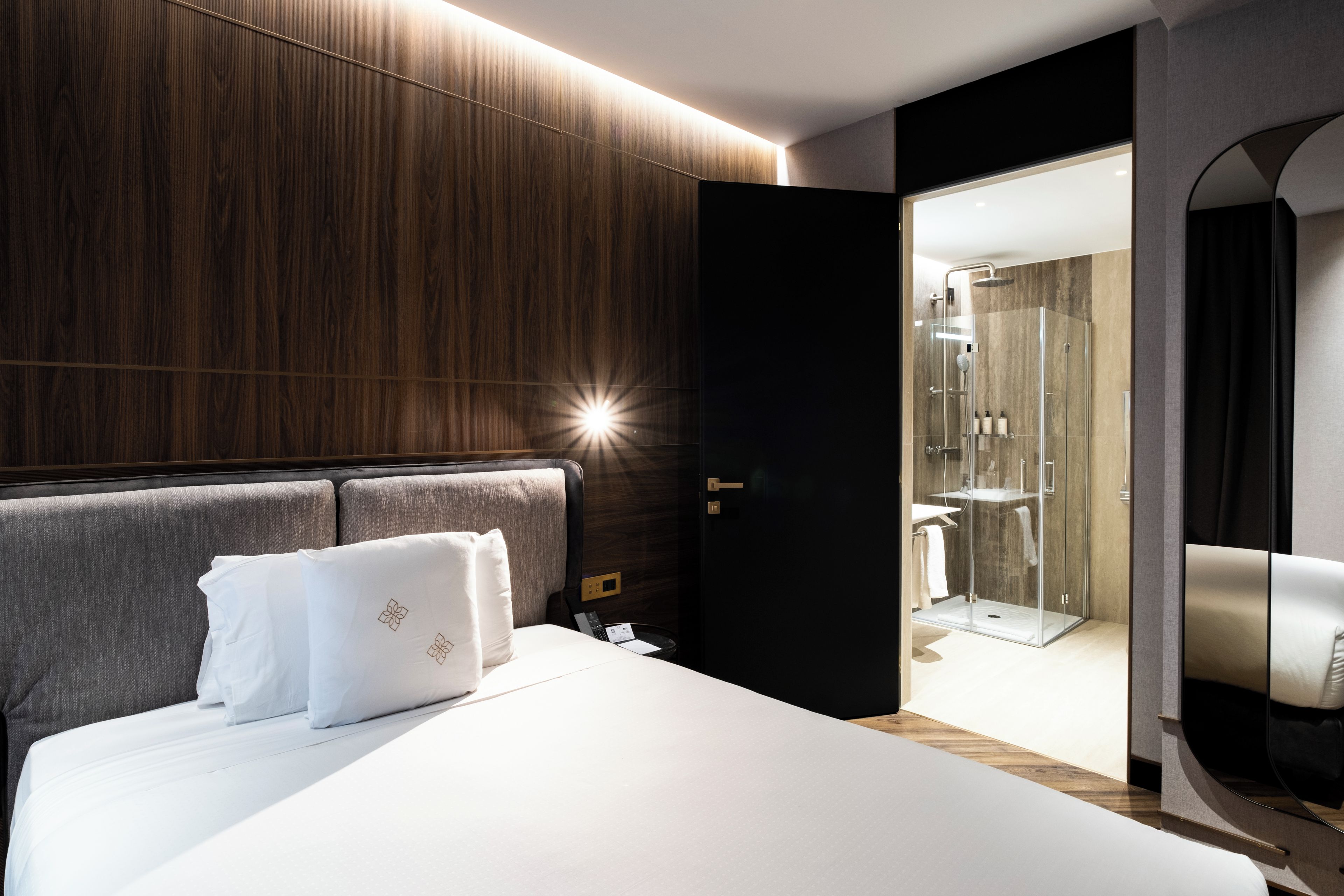 Ein modernes Hotelzimmer mit einem großen Bett, einem hölzernen Kopfteil und einer Duschkabine aus Glas.
