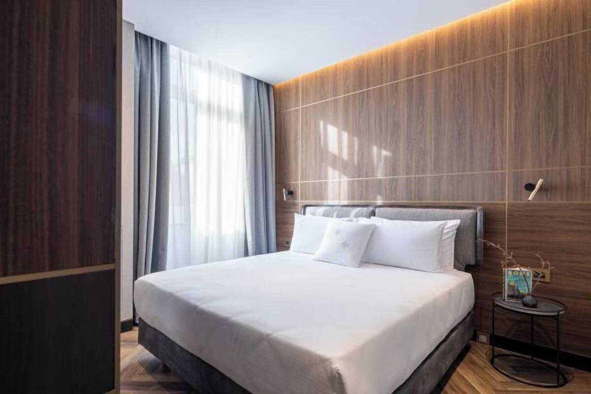 Una camera d'albergo moderna con un letto grande, pareti rivestite in legno, un tavolino e una finestra con tende.