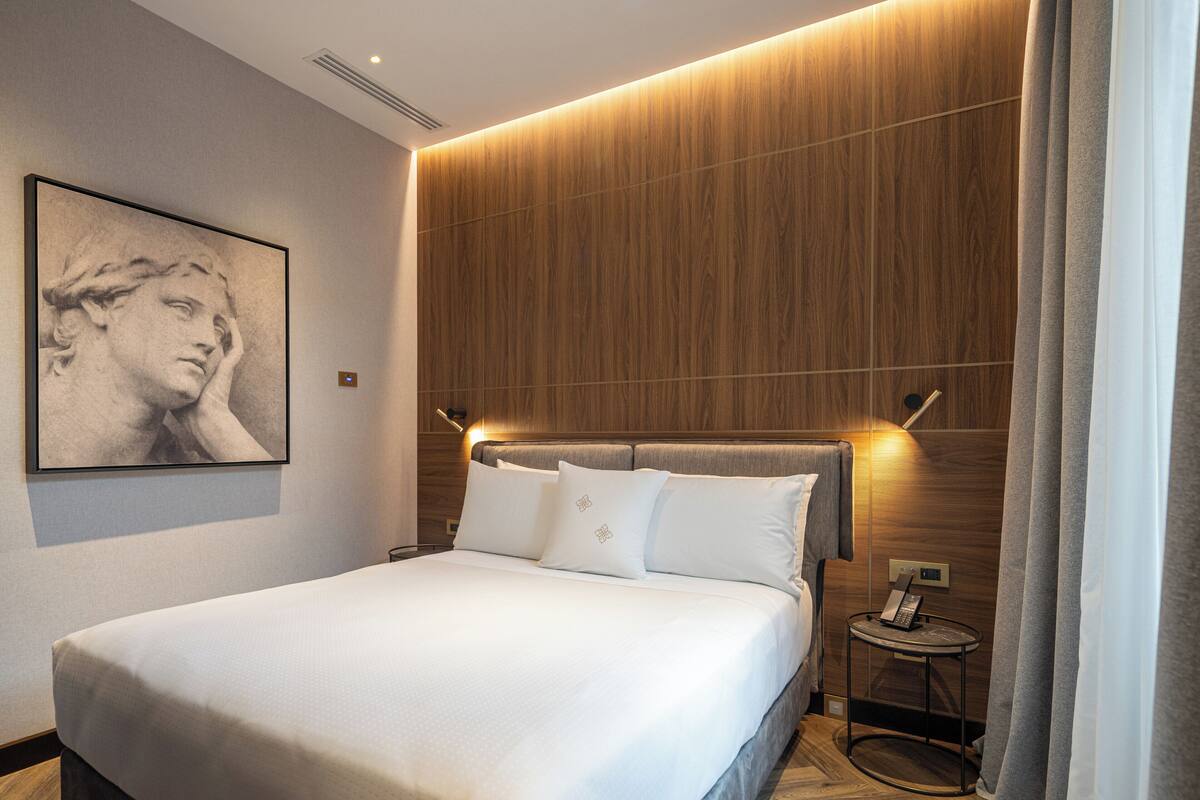 Camera d'albergo moderna con un letto grande, una parete rivestita in legno, un'opera d'arte incorniciata e un telefono sul comodino.