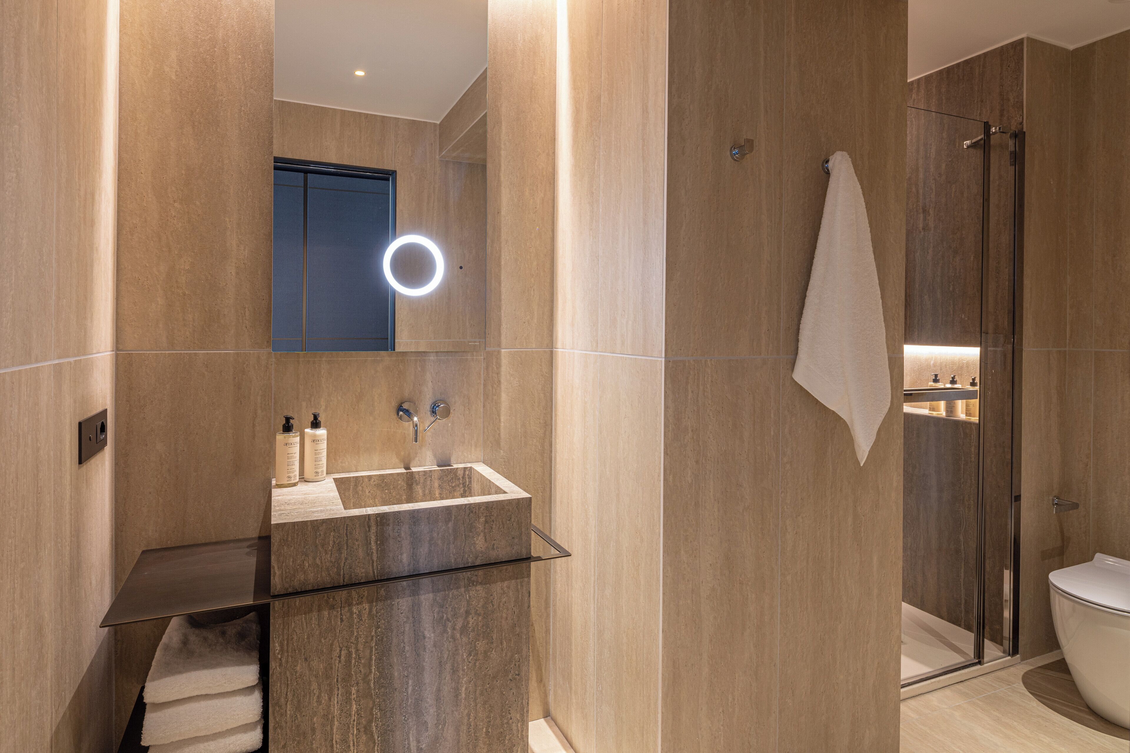 A modern bathroom with a glass sink, a mirror with a ring light, a towel rack, and a glass shower enclosure.