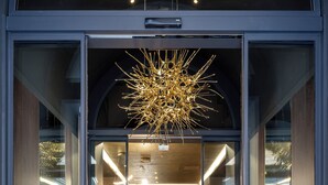 A modern hotel entrance with a glass door, a welcome mat, and a unique chandelier. - Palazzo 4 Fontane 12 (Rome)