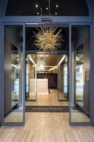 Una entrada de hotel moderna con puerta de cristal, felpudo y una lámpara de araña singular.