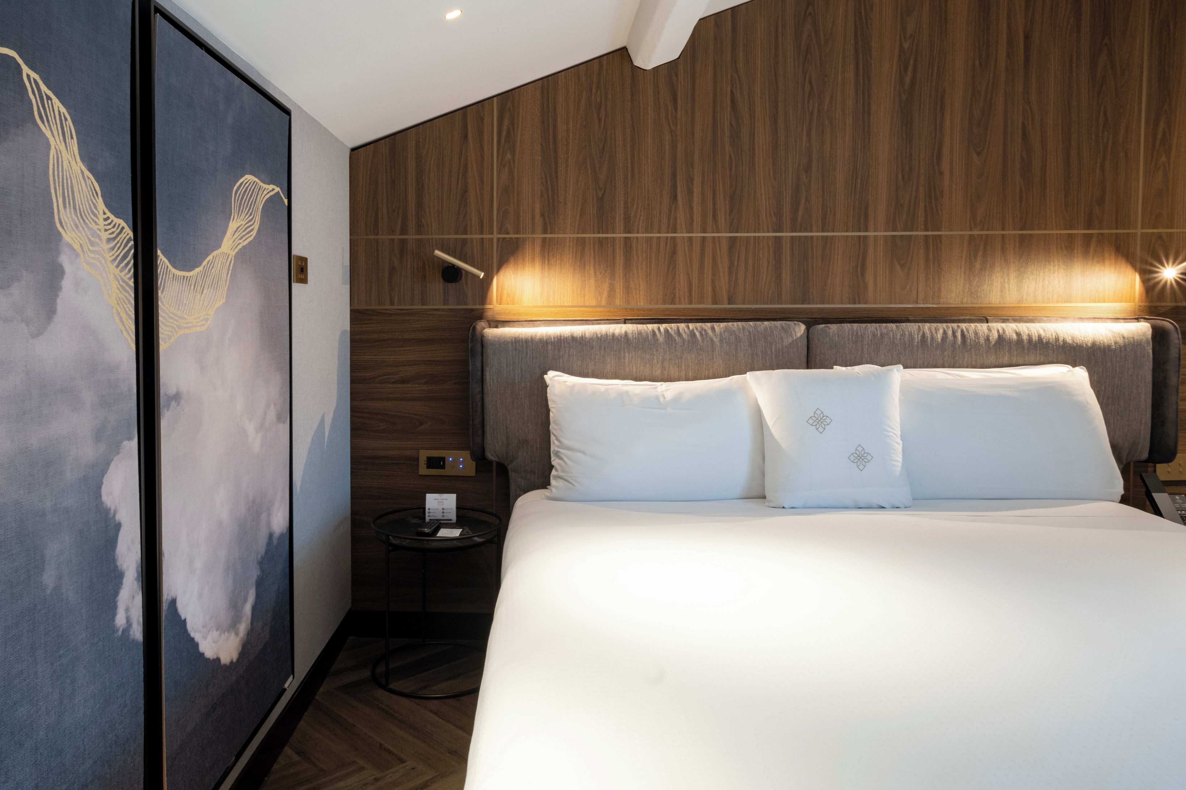 Een moderne hotelkamer met een groot bed, een nachtkastje, een wandlamp en een decoratief paneel.
