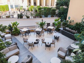 An outdoor seating area with tables and chairs, surrounded by potted plants and a view of a building. - Palazzo 4 Fontane 12 (Rome)