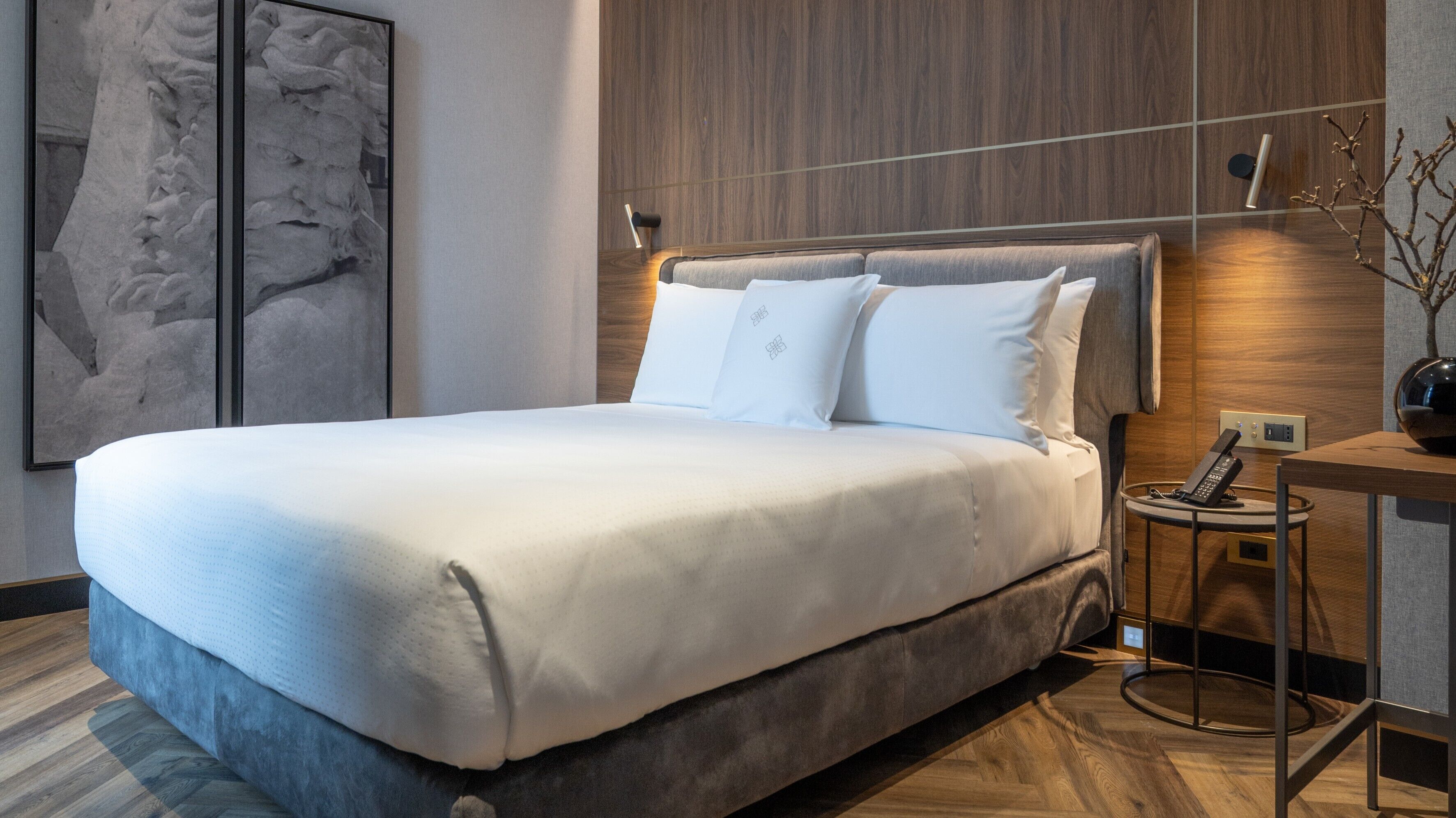 Una habitación de hotel moderna con una cama grande, una mesita de noche con teléfono y una lámpara de pared.