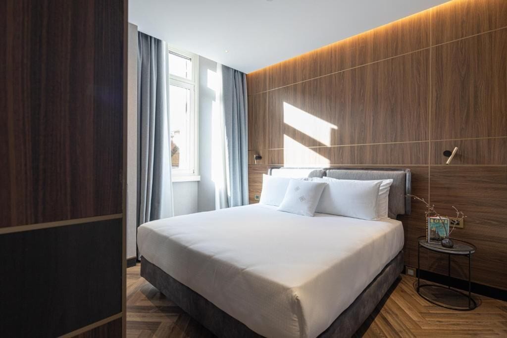 Una moderna camera d'albergo con un letto grande, pareti in legno, un piccolo tavolino e una finestra con tende.