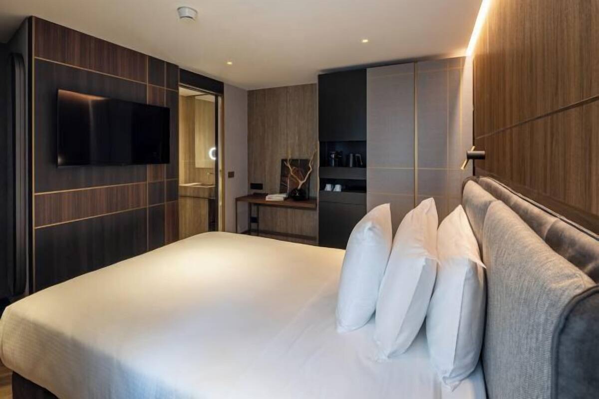 Una camera d'albergo moderna con un letto grande, una televisione a schermo piatto montata a parete e una dispensa integrata con articoli da toilette.
