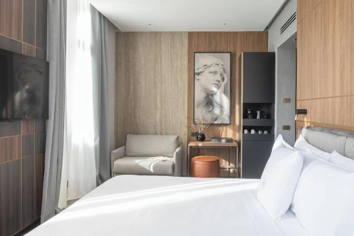 Una camera d'albergo moderna con un letto grande, un divano, una macchina per caffè e una televisione.