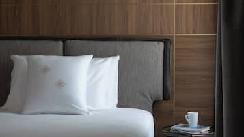 Habitación de hotel con una cama grande, cabecera gris, panel de pared de madera y una mesita con una taza y un libro.