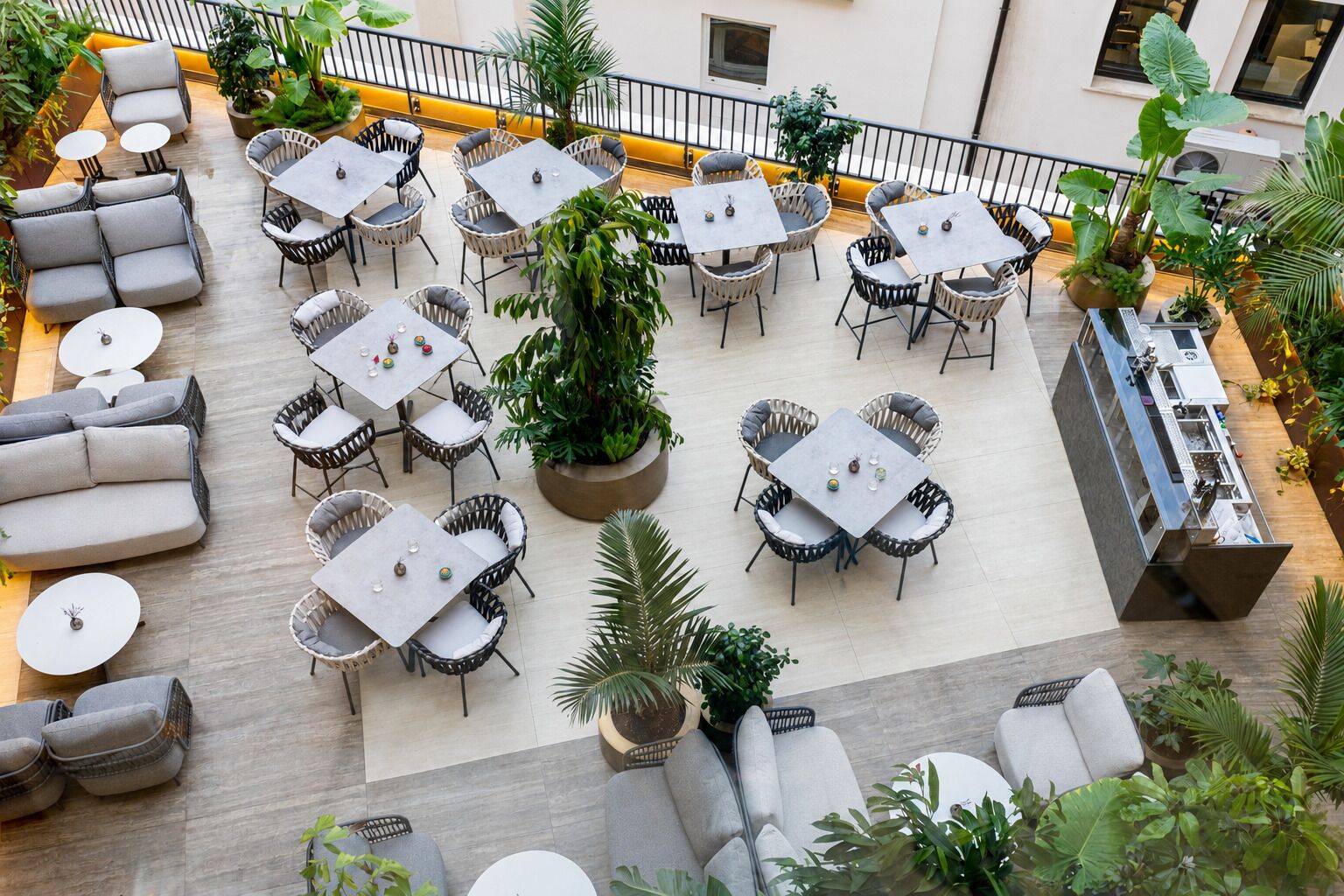 A rooftop terrace with multiple seating areas, including sofas and tables, surrounded by potted plants.