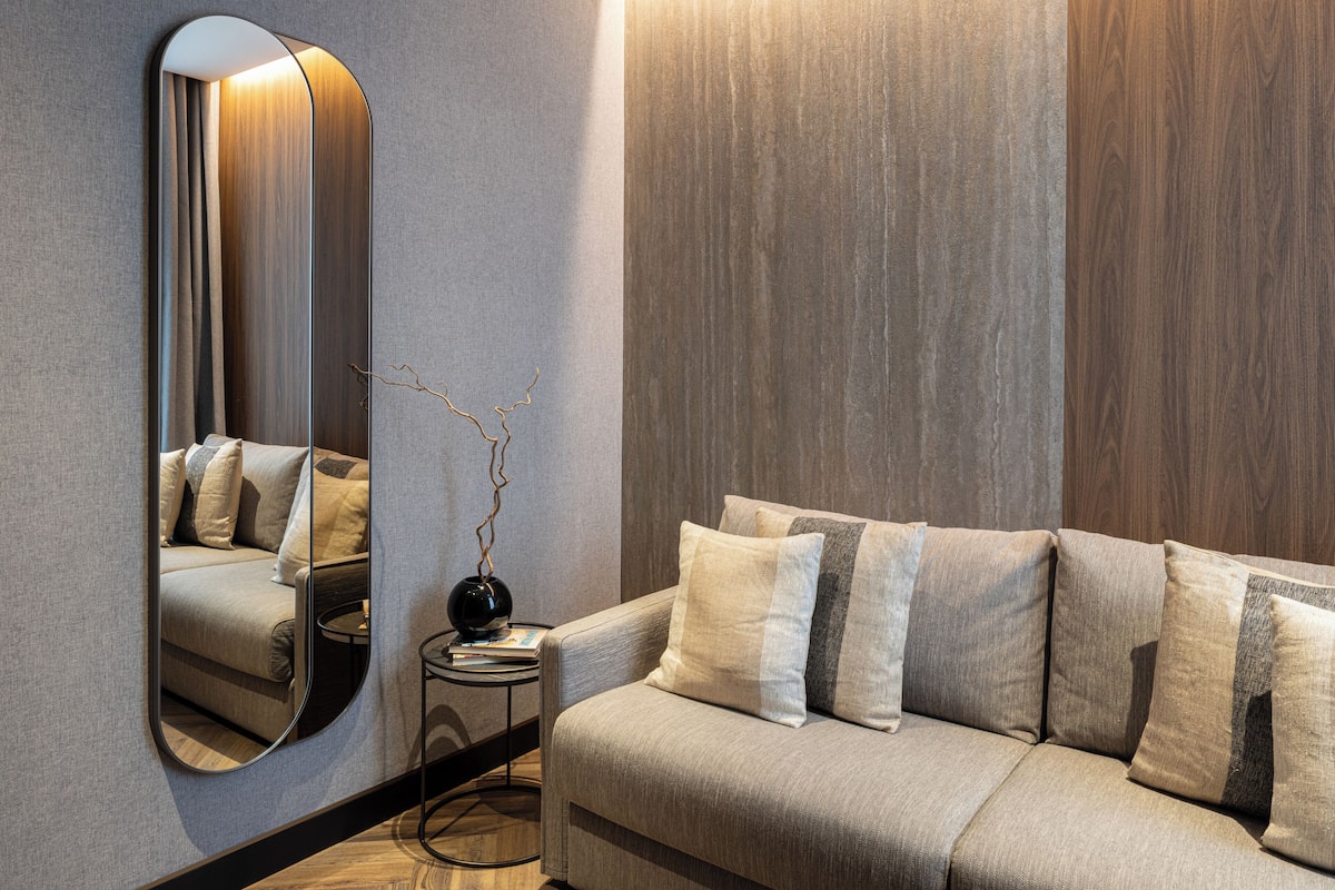 Un salon moderne avec un canapé, un miroir rond, une petite table d’appoint et un vase décoré de branches.