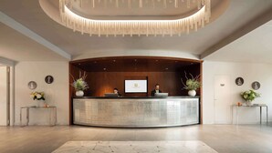 A reception area with a curved desk, two staff members, a large screen, and a modern chandelier. - Hotel American Palace Eur (Rome)